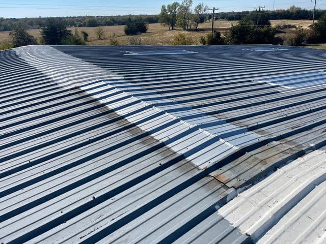 Metal roof with corrugated panels and landscape in the background under clear blue sky.