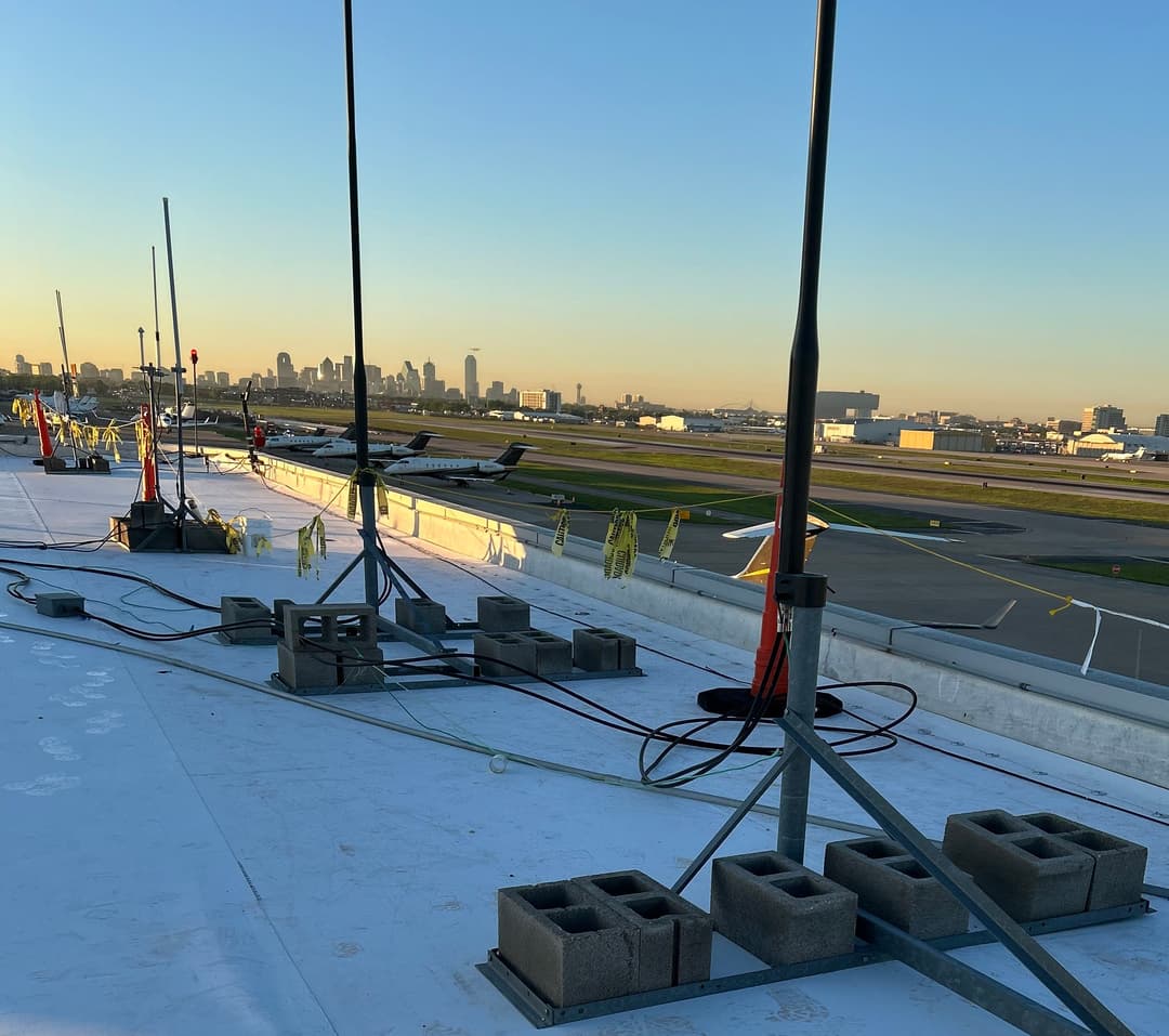 View from rooftop showing antennas and skyline with planes on runway at sunset.