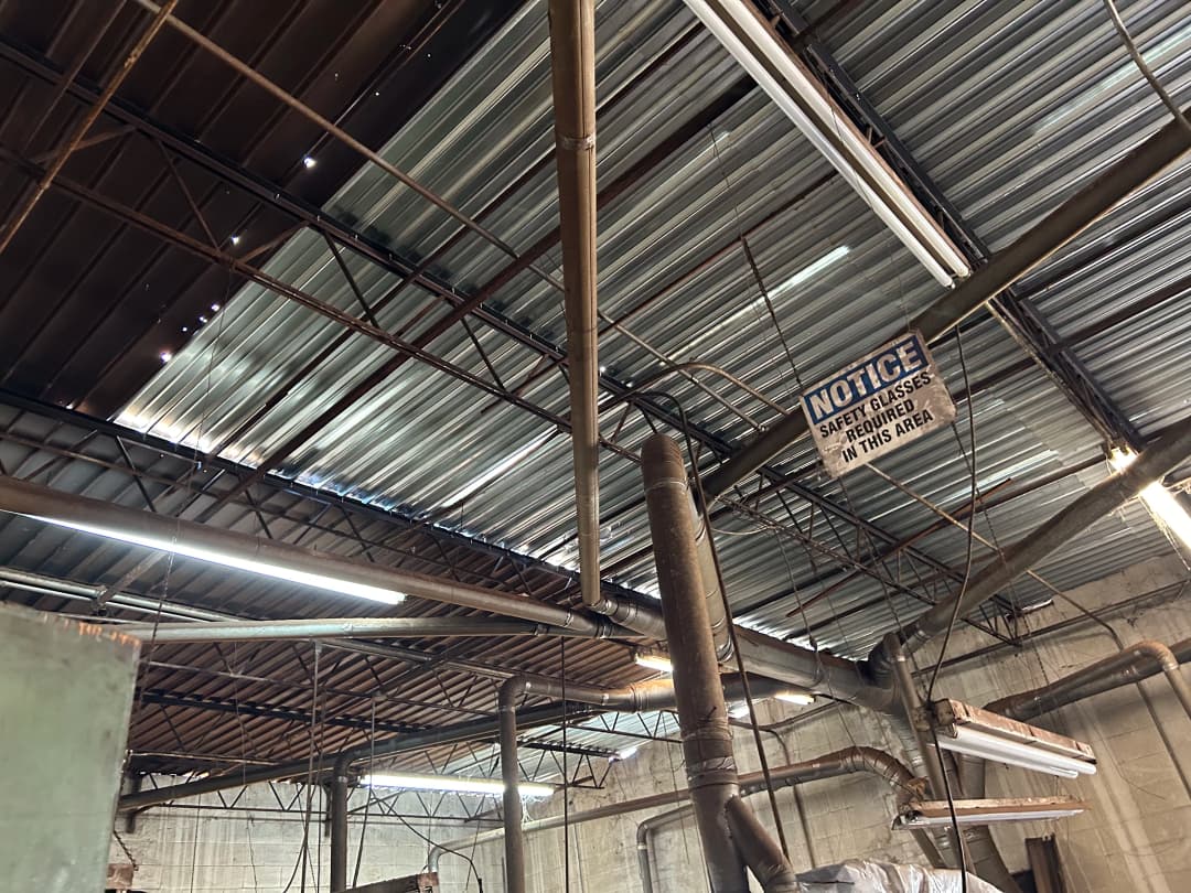 Industrial space with exposed metal beams and safety notice sign on the ceiling.