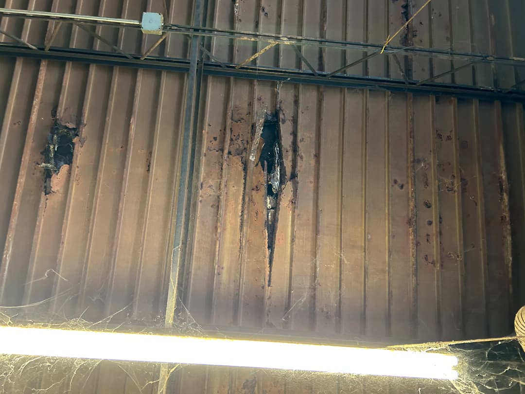 Damaged metal ceiling with cracks and cobwebs, showcasing neglect and structural issues.