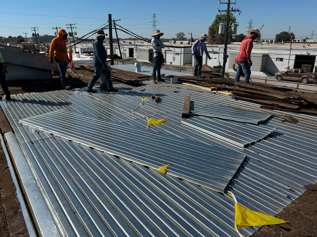 Workers installing metal roofing panels on a construction site under clear blue skies.