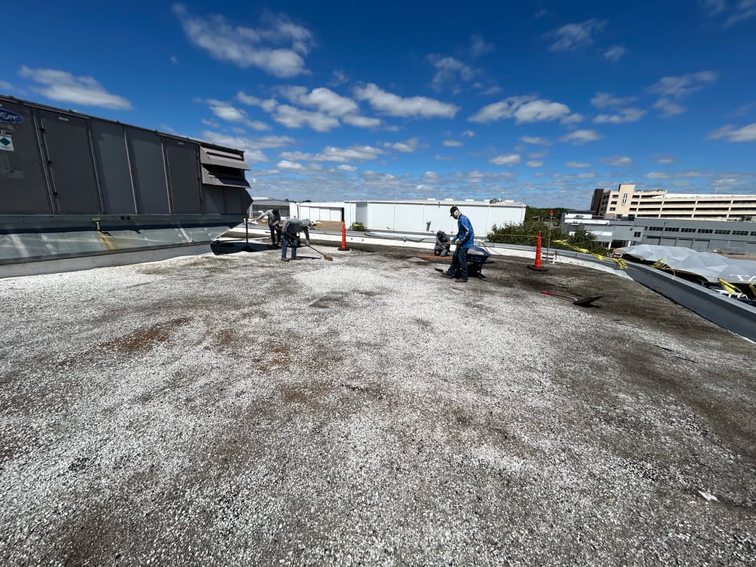 Roof maintenance workers repairing a commercial roof under a clear blue sky.