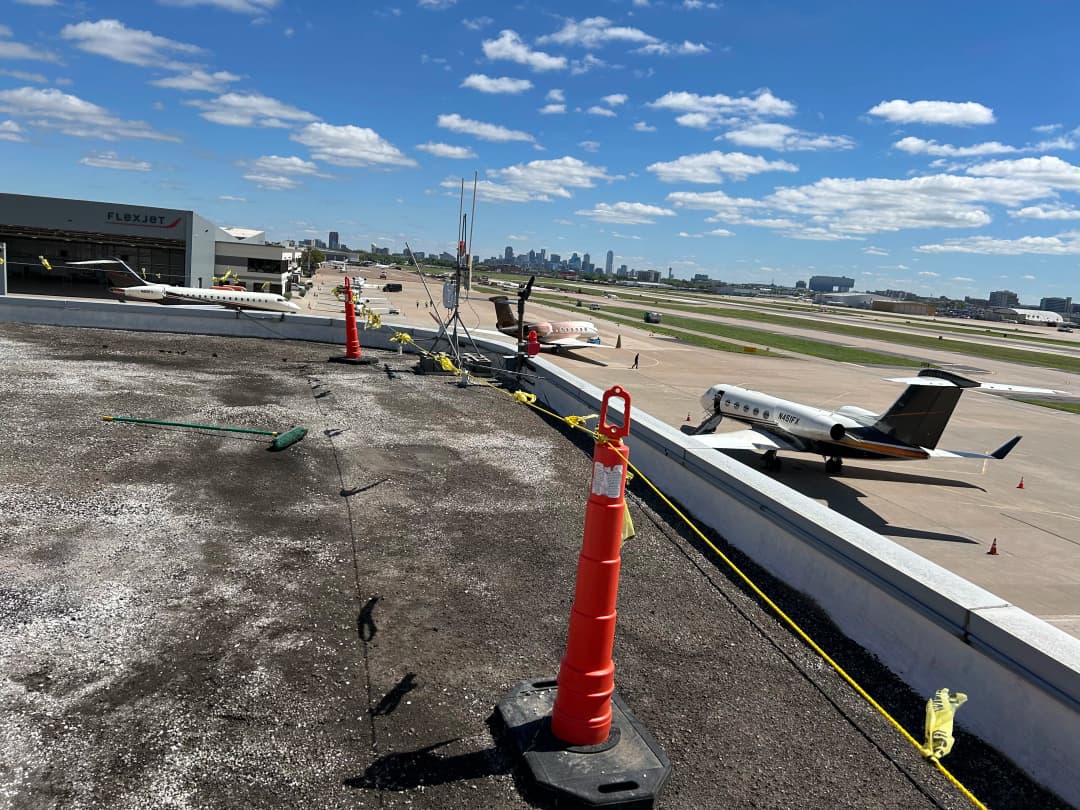 Aerial view of an airport with construction cones and parked private jets under a clear blue sky.