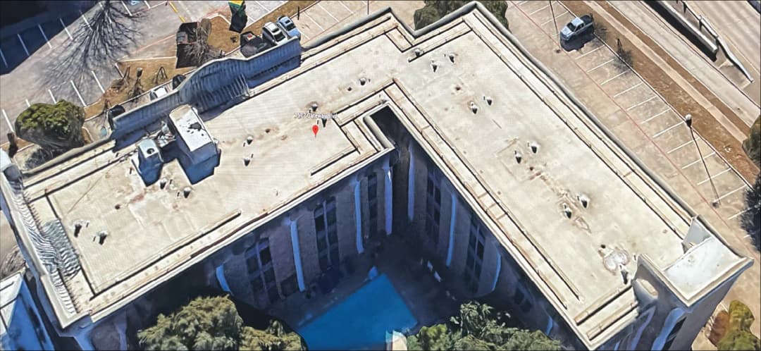 Aerial view of a building roof with a pool and nearby parking lot.