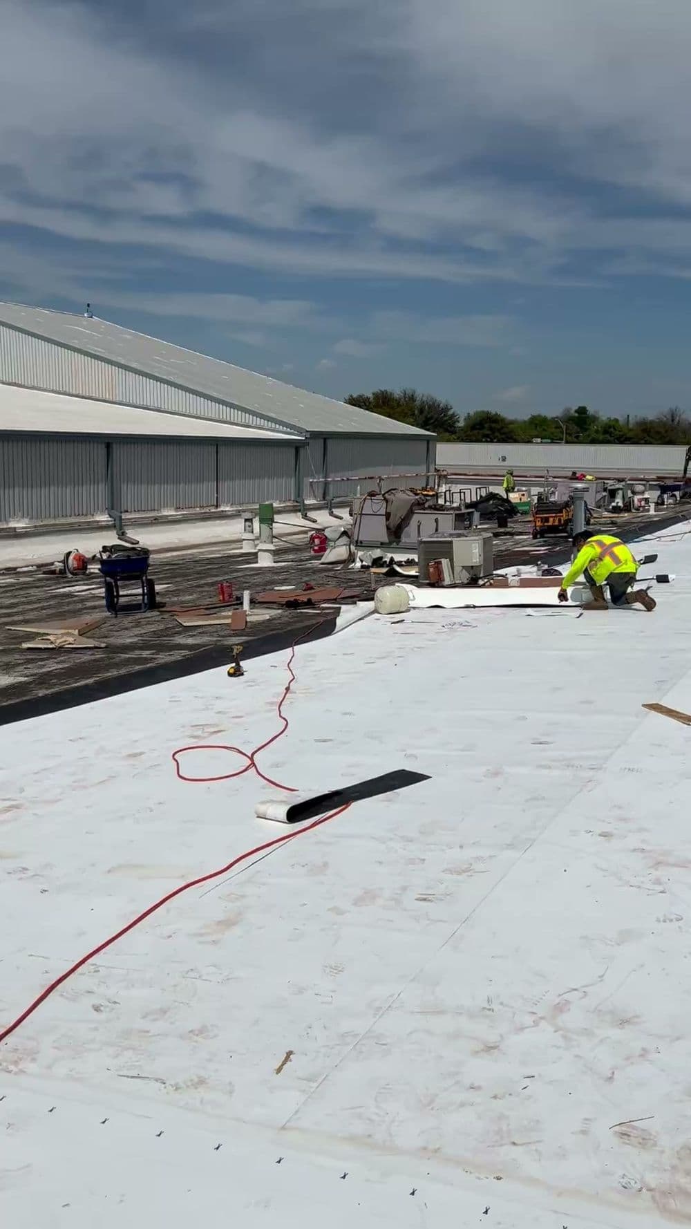 Construction workers applying a white roofing membrane on a commercial building rooftop.