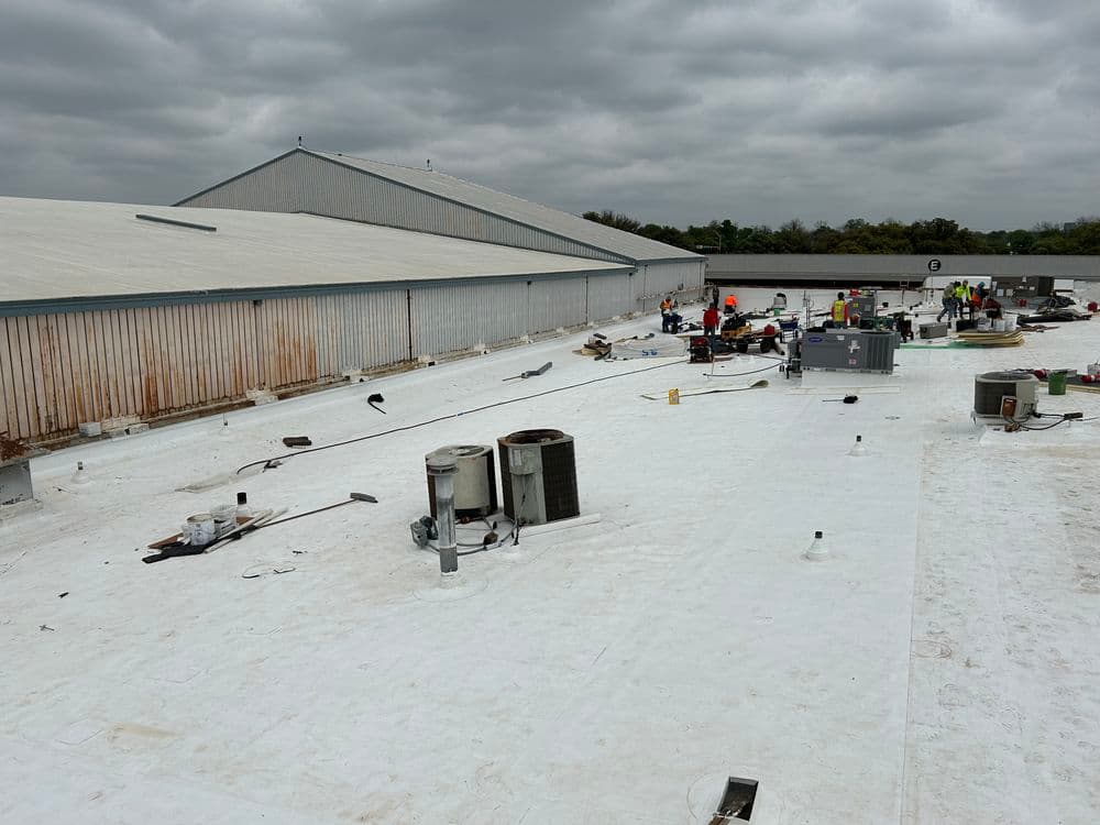 Workers installing a roofing system on a commercial building, with HVAC units visible.