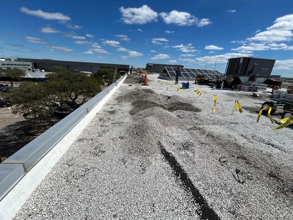 Flat roofing installation with gravel, safety cones, and blue sky in the background.