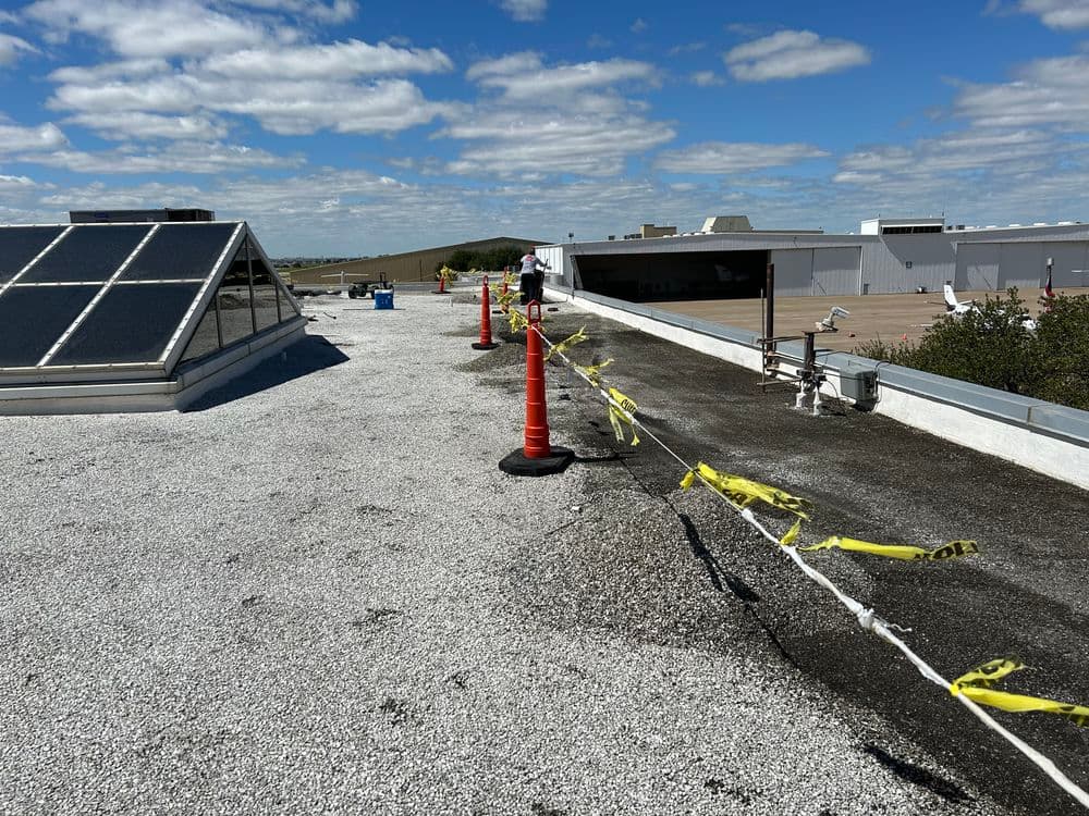 Construction site on a rooftop with orange cones, caution tape, and solar panels under a blue sky.