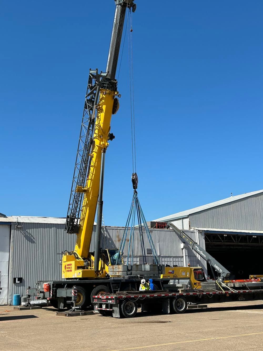 Yellow crane lifting heavy load at construction site under clear blue sky.