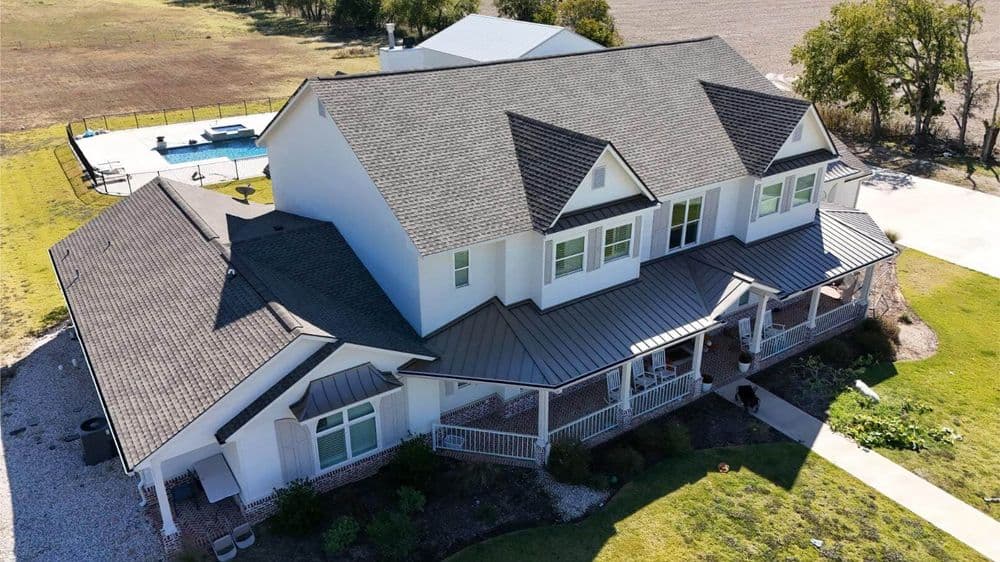 Aerial view of a modern white house with a large porch, pool, and expansive landscape.