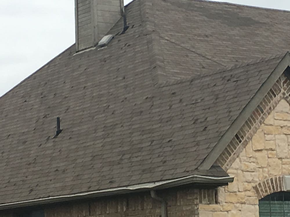 Roof with shingles and chimney on a residential stone house exterior.