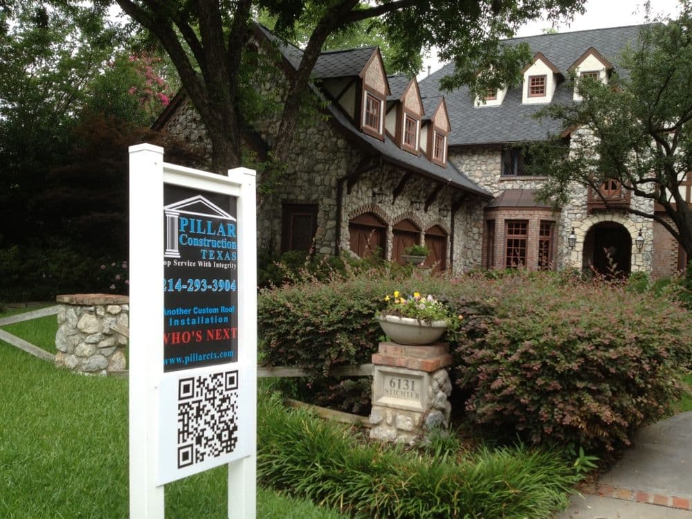 Custom stone house with landscaping and construction sign in front, featuring a QR code.
