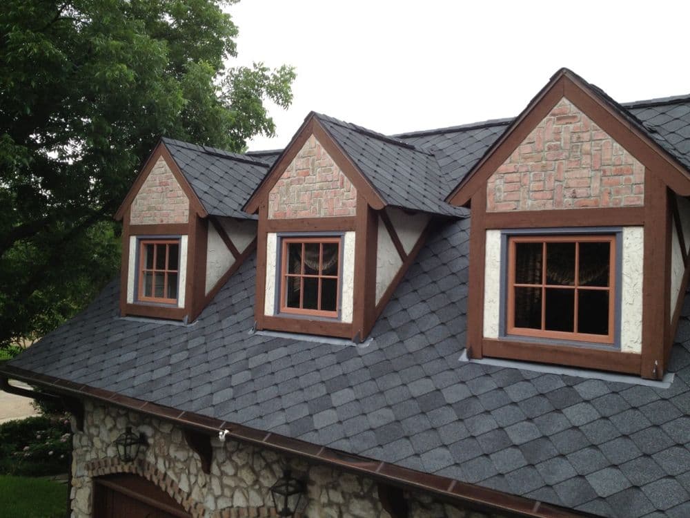 Charming roof design with three dormers, stone accents, and dark shingles. Ideal home architecture.