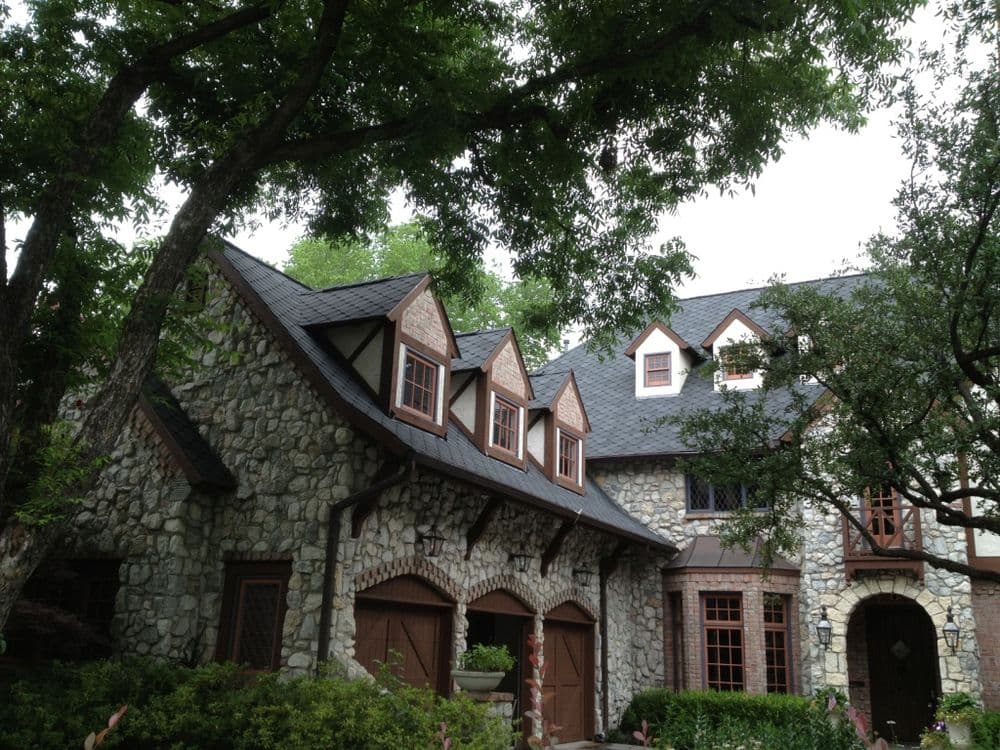 Beautiful stone house with Tudor-style architecture surrounded by lush green trees.