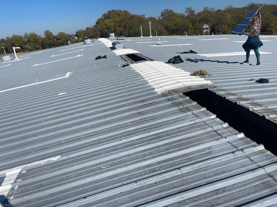 Person repairing a metal roof with holes, surrounded by tools and clear blue sky.